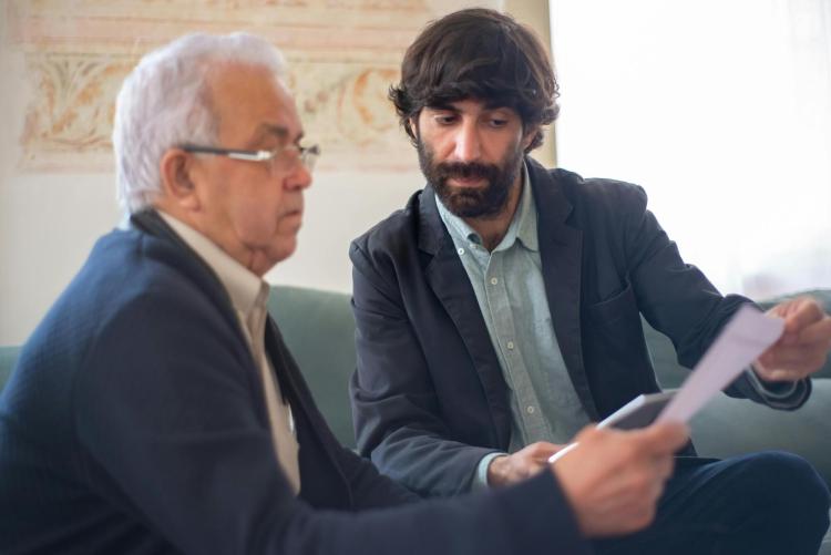 2 men of different ages sitting next to each other, reviewing paperwork
