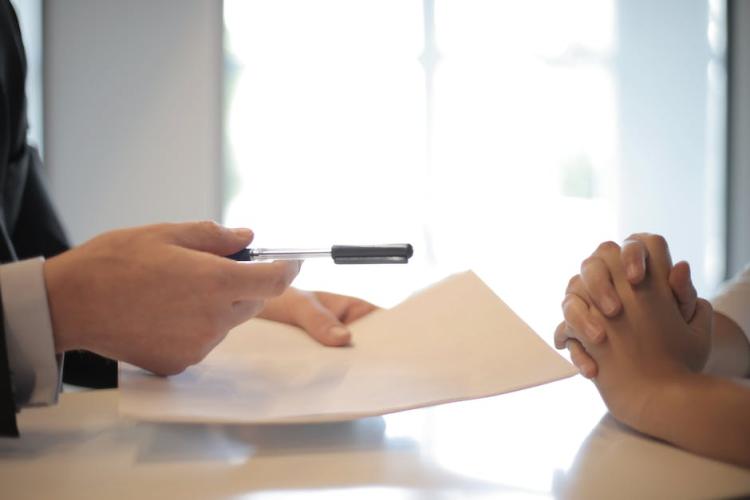 Hands of a person offering a pen and paper, to be signed, to another person's hands